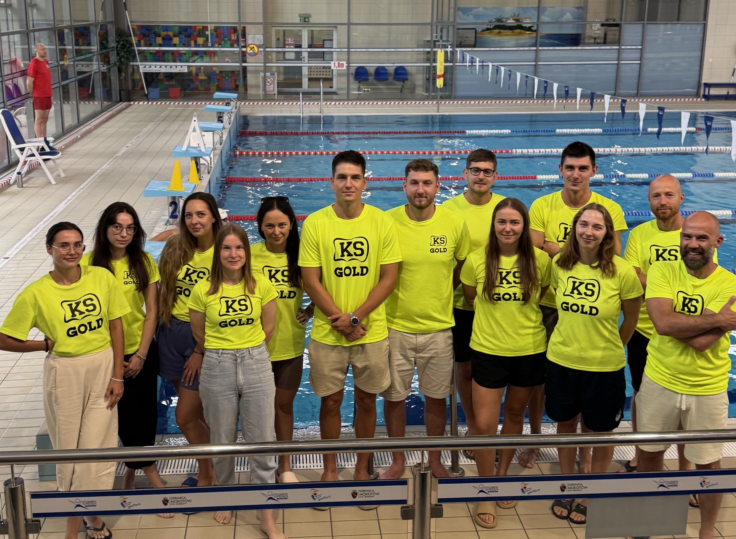 Grupa w żółtych koszulkach przy basenie.